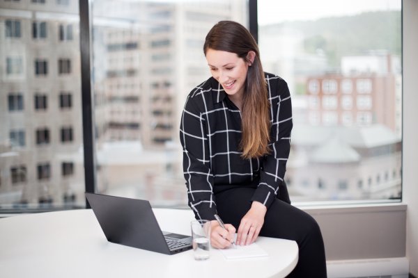 team member checking info on a laptop and writing insights on a piece of paper 