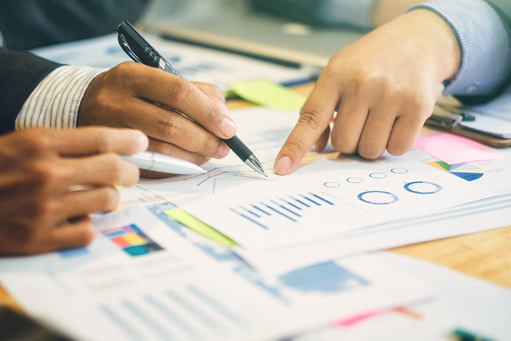 A person's hands using a pen to point at a paper with different types of charts on it.
