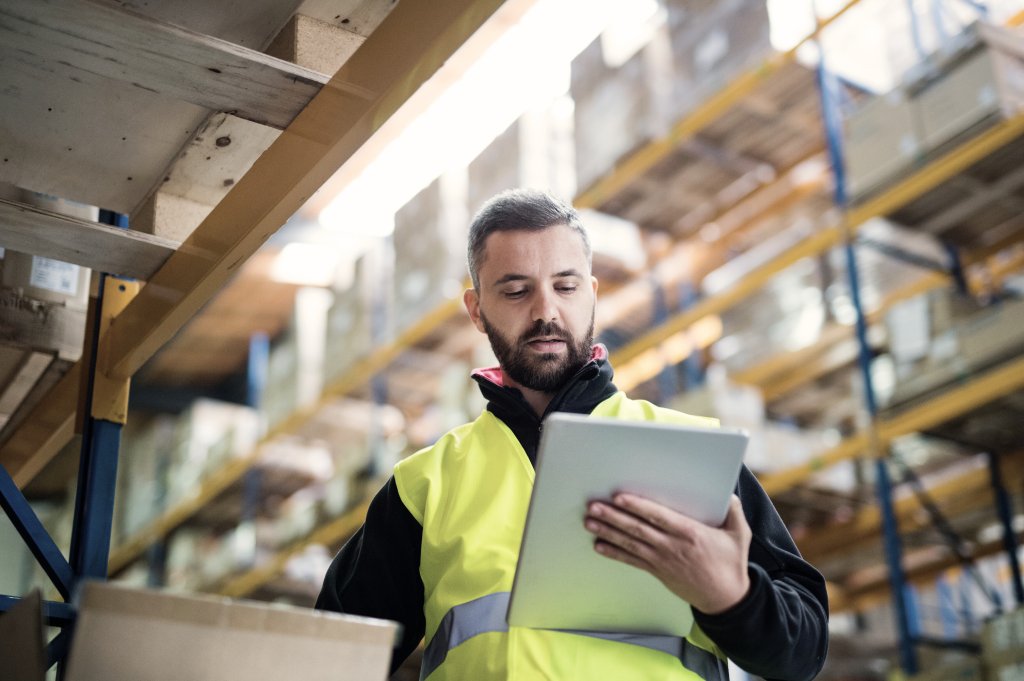 Man wearing a high visibility vest in a warehouse looking at a clipboard